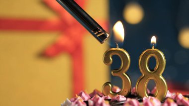 Birthday cake number 38 golden candles burning by lighter, background gift yellow box tied up with red ribbon. Close-up