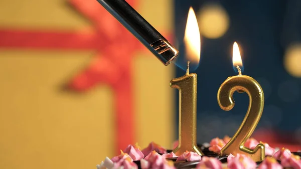 Tort de ziua de naștere numărul 12 lumânări de aur care ard de brichetă, cadou de fundal cutie galbenă legată cu panglică roșie. Close-up — Fotografie, imagine de stoc