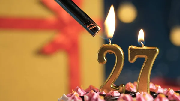 Tort de ziua de naștere numărul 27 lumânări de aur care ard de brichetă, cadou de fundal cutie galbenă legată cu panglică roșie. Close-up — Fotografie, imagine de stoc