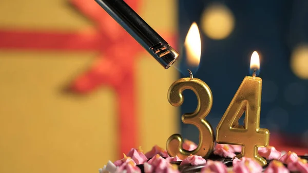 Tort de ziua de naștere numărul 34 lumânări de aur care ard de brichetă, cadou de fundal cutie galbenă legată cu panglică roșie. Close-up — Fotografie, imagine de stoc