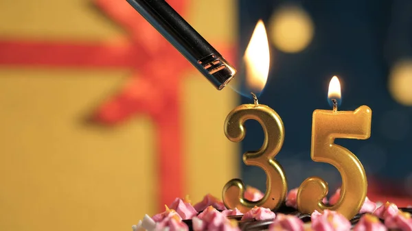 Tort de ziua de naștere numărul 35 lumânări de aur care ard de brichetă, cadou de fundal cutie galbenă legată cu panglică roșie. Close-up — Fotografie, imagine de stoc