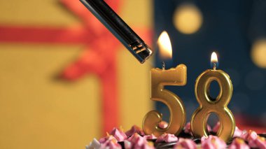 Birthday cake number 58 golden candles burning by lighter, background gift yellow box tied up with red ribbon. Close-up