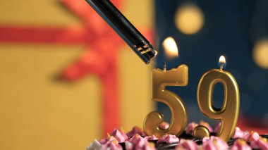 Birthday cake number 59 golden candles burning by lighter, background gift yellow box tied up with red ribbon. Close-up