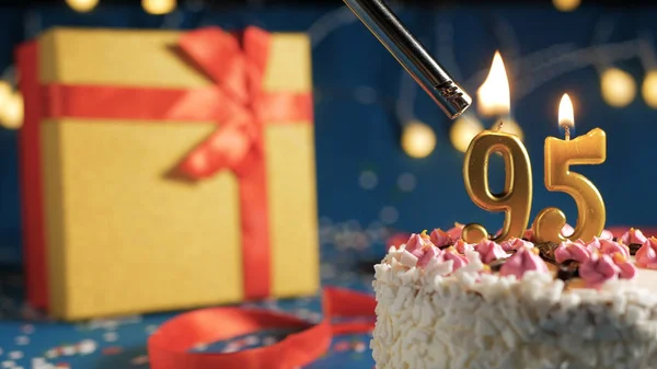 Gâteau d'anniversaire blanc numéro 95 bougies dorées brûlant par briquet, fond bleu avec des lumières et cadeau boîte jaune attaché avec ruban rouge. Gros plan — Photo