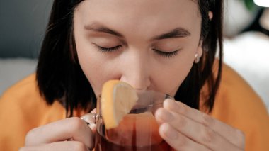 Öndeki kız siyah çay içiyor. Çekici genç kadın hasta ve yatakta otururken limonlu çay içiyor. Grip, grip, boğaz ağrısı, burun akut solunum hastalığı konsepti. Kapat.