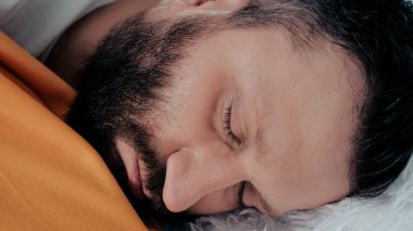 Adamın ateşi var. Kafkasyalı genç adam titreyerek yatağa uzanıyor. Soğuk algınlığı, grip, soğuk terleme, virüs, akut solunum hastalığı, titreme konsepti. Yakın plan.