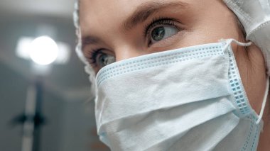 Cerrahi maskeli kız cerrah monitörlere ya da asistanlara bakar. Ameliyat, pratisyen, ameliyathane, ameliyat, organ nakli, tıp konsepti. Yakın çekim görünümü