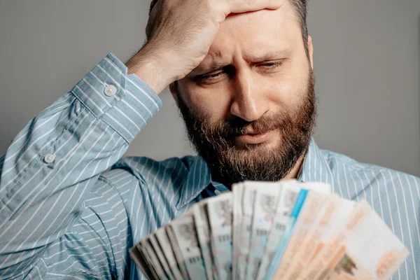 Russian ruble falling inflation concept. Portrait of man looks at bundle of money rubles holding his head and expresses emotions of frustration, pain, hopelessness. Close-up view