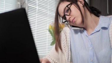 Mutfakta gözlüklü yorgun bir kız iki eliyle dizüstü bilgisayara bir şeyler yazarken biriyle telefonda rahatsız edici konuşmalar yapıyor. İş görüşmesi konseptinde serbest çalışan bir kız.