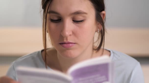 Kız kitap okuyor. Genç beyaz kadın akşamları yatakta oturur ve yatmadan önce dikkatlice kitap okur, sayfayı çevirir. Yakın plan. — Stok video