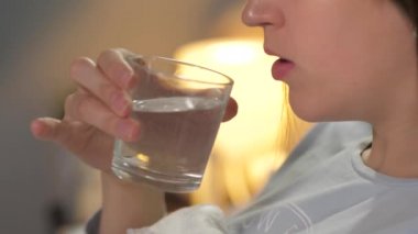 Kız yatmadan önce şeffaf camdan yatmadan önce su içer. Yakın plan.