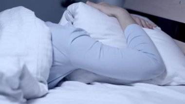 Gürültücü komşular, kabus kavramı. Kız geceleri yatakta tek başına başını yastıkla örtüyor. Yakın plan.