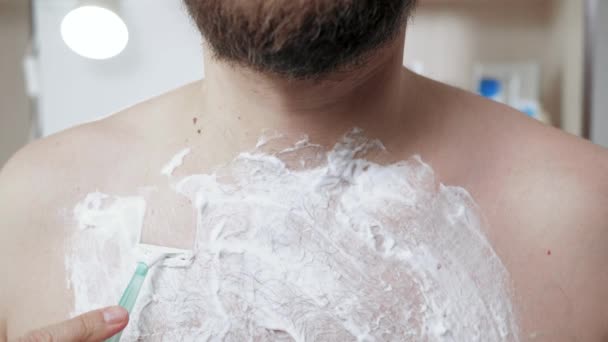 Hij scheert zijn borst. Middelbare leeftijd baard blanke man drijft wegwerp scheermachine over zijn borst met het verspreiden van schuim. Close-up — Stockvideo