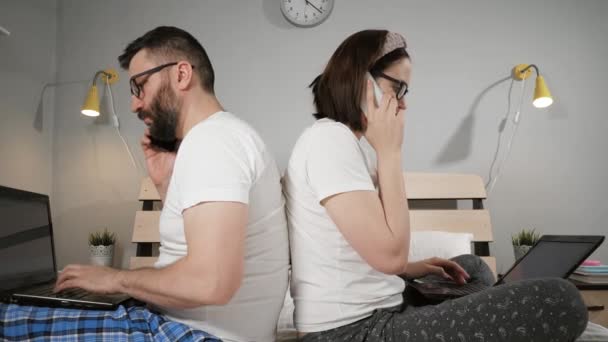 Thuis werken, freelance concept. Man en vrouw op bed in de slaapkamer, rug aan rug, tijdens het werk, typen op laptop toetsenbord, praten op mobiele telefoon. Close-up — Stockvideo