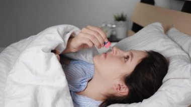 Hasta, burnu akan kadın battaniyenin altında yatar ve burnunu pipetten damlatır. Soğuk algınlığı, grip, alerji, romatizma, hipotermi, kuru hava kavramları. Yakın plan.