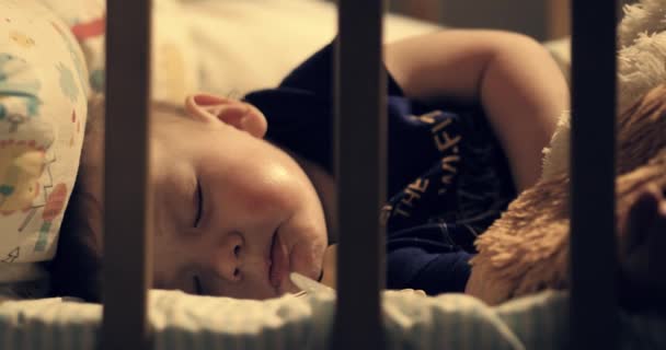 Дитина прокидається вночі в дитячому ліжечку і плаче. Тепле світло від лампи падає на дитину. Крупним планом — стокове відео