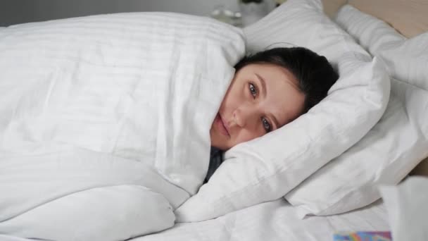 Mujer shills en la cama se envuelve en manta y cierra los ojos, ella es fría. Frío, gripe, conceptos de fiebre. Movimiento lento — Vídeo de stock