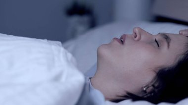 Kız horluyor. Burun tıkanıklığı, apne, burun kıvrımı, yorgunluk konsepti. Genç ve çekici bir kadın yatakta ağzı açık uyuyor. Yakın plan.