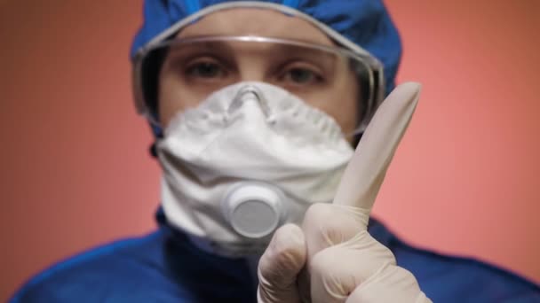 Meisje met masker met beschermend pak en bril kijkend naar de camera en verbiedt wijzende vinger. Waarschuwing, epidemie, pandemie, COVID-19, ziektebestrijding, infectierisico concept. Sluiten. — Stockvideo