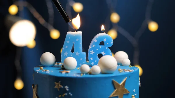 Birthday cake number 46 stars sky and moon concept, blue candle is fire by lighter. Copyspace on right side of screen. Close-up view