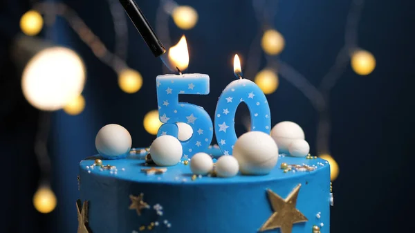 Birthday cake number 50 stars sky and moon concept, blue candle is fire by lighter. Copyspace on right side of screen. Close-up view
