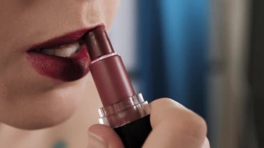 Kız dudaklarını boyuyor. Dudaklarına parlak ruj süren genç bir kadının makro çekimi. Güzellik uzmanı, evde tek başına makyaj. Yakın plan.