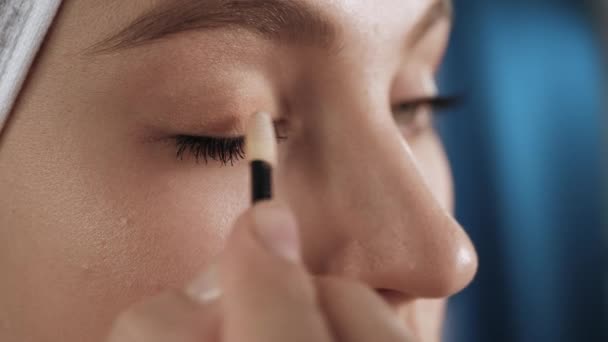 A menina põe sombra de olho de pálpebras. Mulher atraente com toalha na cabeça no banheiro olha no espelho e coloca sombra na pele ao redor dos olhos. Esteticista, maquiagem em casa sozinho conceito. Close-up — Vídeo de Stock