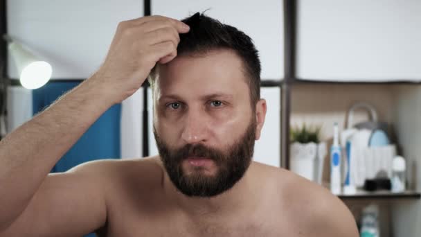 Людина махає своїм волоссям. Молодий привабливий кавказький хлопець у ванній мацає волосся перед дзеркалом. Гігієна, догляд за волоссям, зачіска, ідея свіжості. Підсумок. — стокове відео