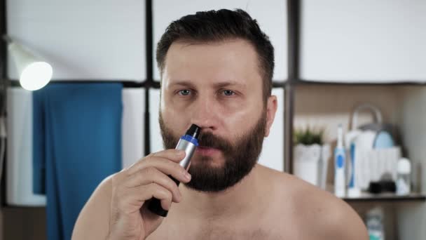 Muž stříhá chloupky v nose. Atraktivní mladý muž v koupelně se podívá do zrcadla a pomocí trimru se řízne do nosu. Hygiena, čerstvost. Detailní záběr — Stock video
