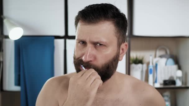 L'homme se brosse les dents. attrayant barbu gars dans la salle de bain regarde dans le miroir et se brosse les dents avec une brosse à dents. Hygiène, concept de fraîcheur. Gros plan — Video