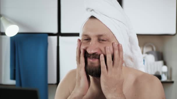 O homem admira-se. Travesty, cara atraente com toalha na cabeça no banheiro olha no espelho e admira sua beleza. Close-up — Vídeo de Stock