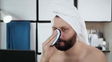 Adam yüzünü süngerle yıkıyor. Travesty, genç beyaz adam banyoda aynaya bakar ve yüzünü süngerle siler. Yakın plan.