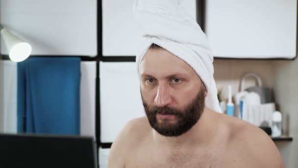 Мужчина делает массаж лица. Трэвити, привлекательный бородатый парень в ванной с полотенцем на голове делает себе массаж рук в области носа. Крупный план — стоковое видео