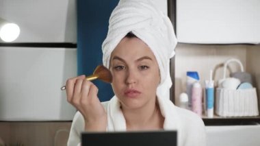 Yüzüne sürtünen kız cilt için parlıyor. Banyoda kafasında havlu ve bornoz olan çekici bir kadın cildine fosforlu kalem ya da bronzlaştırıcı sürüyor. Güzellik uzmanı, evde tek başına makyaj. Yakın plan.