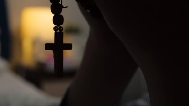 Prière. Les mains féminines tiennent un chapelet avec crucifix sur fond de lampe jaune vif dans la chambre. Vue rapprochée 