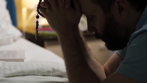 男人在祈祷长胡子的男人坐在床边卧室的地板上 手里拿着十字架 做着祈祷 — 图库视频影像