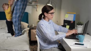Kız evde internet üzerinden çalışıyor. Genç kadın anne yatak odasında oturuyor dizüstü bilgisayarda klavyeyle yazı yazıyor arka planda küçük çocuk yatakta ve babasıyla oynuyor. Yakın çekim ve Yavaş Hareket