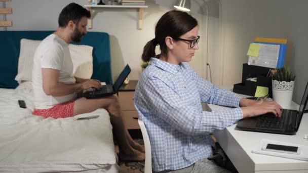 부부는 온라인으로 집에서 일합니다 남자는 차림으로 침대에 노트북 키보드 무언가를쓰고 — 비디오