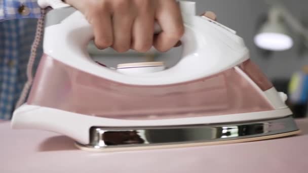 Девушка гладит бельё. Женские руки перемещают утюг над розовыми кроватями на гладильной доске в квартире — стоковое видео
