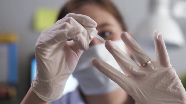 Girl in mask and gloves paints nails. Young woman in latex white gloves and surgical mask on her face paints her fingernails with nail polish over gloves. Pandemic Parody Concept — Stock Video