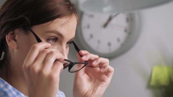 Flickan tar på sig glasögon. Närbild av ung kvinna på arbetsplatsen i kontor eller lägenhet som sätter på glasögon för syn eller för att arbeta med dator — Stockvideo
