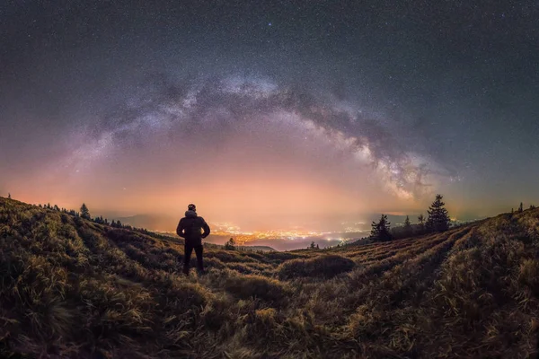 Person looks at the city and Milky Way glowing in the sky