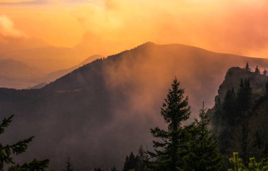 The rising sun illuminates the clouds everywhere between the mountains