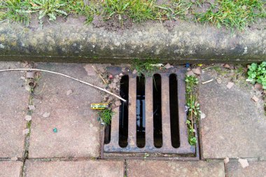 Sewer well in the sidewalk tiles and grass