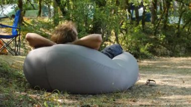 Güneşli bir günde kamp yaparken hava yastığında dinlenen bir adam.