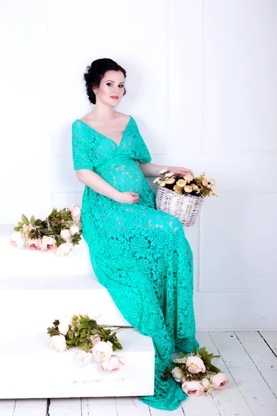 Těhotná žena sedí s košíkem květin — Stock fotografie