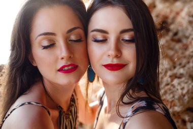 Kumsalda, kayaların yanında bronzlaşmış genç bir kadın.