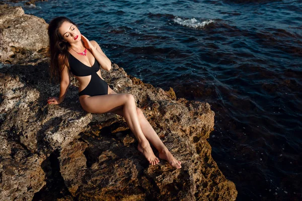 A fiatal, gyönyörű, napbarnított nő a parton, a sziklák közelében. — Stock Fotó