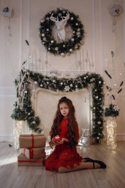 Şöminenin yanında oturan parlak kırmızı elbiseli bir kız.