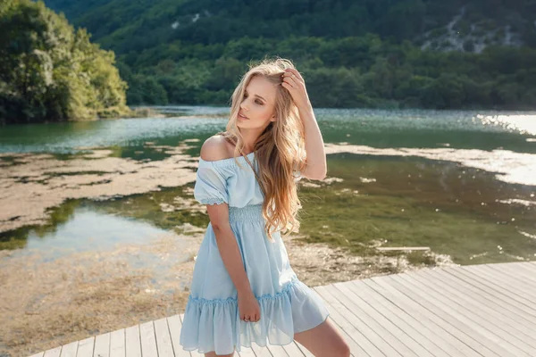 Young woman in blue dress standing alone on footbridge and staring at lake. Mist over water. Chilly morning. — Stock Photo, Image